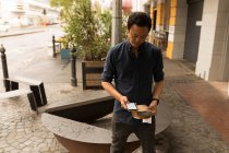 Geschäftsmann hält Paket während Handynutzung im Straßencafé — Stockfoto