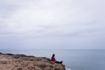Donna che si rilassa su una roccia in spiaggia in una giornata di sole — Foto stock
