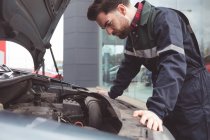 Мужчина-механик, обслуживающий автомобиль в ремонтном гараже — стоковое фото