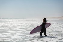 Surferin steht an einem sonnigen Tag mit Surfbrett am Strand — Stockfoto