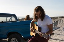 Homem tocando guitarra na praia em um dia ensolarado — Fotografia de Stock