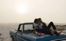Couple ayant de la bière sur un capot de camionnette dans la plage — Photo de stock