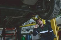 Meccanico maschio che esamina una macchina con torcia in garage di riparazione — Foto stock