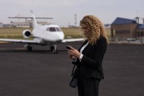 Schöne Geschäftsfrau benutzt Handy am Terminal — Stockfoto