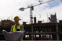Female architect checking blueprint at construction site — Stock Photo