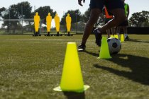 Soccer player dribbling the ball through cones in sports field — Stock Photo