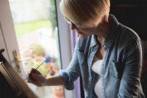 Artista feminina pintando em uma tela com um pincel em casa — Fotografia de Stock