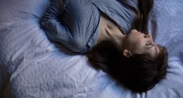 Thoughtful woman lying on bed in bedroom — Stock Photo