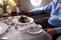Sección media del hombre de negocios comiendo mientras viaja en jet privado - foto de stock