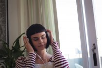Jovem mulher ouvindo música em fones de ouvido em casa — Fotografia de Stock