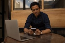 Бизнесмен с помощью мобильного телефона с ноутбуком на столе в кафе — стоковое фото