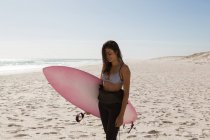 Surfista feminina de pé com prancha na praia em um dia ensolarado — Fotografia de Stock