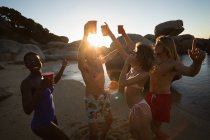 Grupo de amigos divirtiéndose en la playa al atardecer - foto de stock