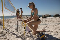 Female volleyball coach tying volleyball net on the beach — Stock Photo