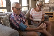 Seniorenpaar überprüft Blutdruck mit Blutdruckmessgerät im heimischen Wohnzimmer — Stockfoto