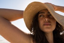 Femme en chapeau debout à la plage par une journée ensoleillée — Photo de stock