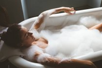 Mulher tomando um banho de espuma no banheiro em casa — Fotografia de Stock