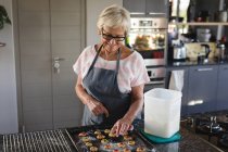 Старшая женщина готовит печенье на кухне дома — стоковое фото