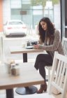 Mulher usando telefone celular enquanto toma café na cafeteria — Fotografia de Stock