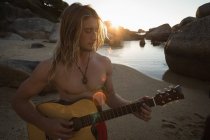 Человек, играющий на гитаре на пляже в сумерках — стоковое фото