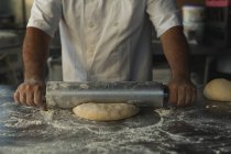 Sección media del panadero masculino usando rodillo en panadería - foto de stock