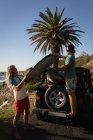 Amigos varones quitando la tabla de surf del jeep en la playa - foto de stock