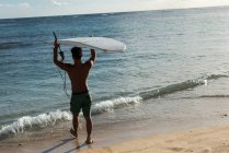 Задній вид чоловічого серфер, прогулянки з дошки для серфінгу на пляжі — стокове фото