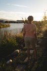 Rückansicht einer Seniorin, die an einem sonnigen Tag in Ufernähe spaziert — Stockfoto