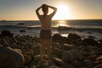Visão traseira da mulher em pé na rocha ao pôr do sol — Fotografia de Stock