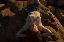 Femme se détendre sur le rocher à la plage pendant le coucher du soleil — Photo de stock