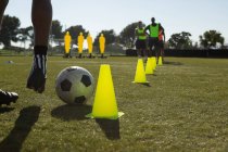 Jugador de fútbol driblando la pelota a través de conos en el campo de deportes - foto de stock