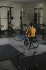 Uomo handicappato sulla sedia a rotelle che si allena con le corde da battaglia in palestra — Foto stock