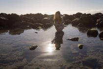 Frau kauert an einem sonnigen Tag im flachen Wasser — Stockfoto