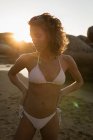 Donna in piedi con le mani sul fianco in spiaggia al tramonto — Foto stock