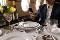 Середина бізнесмена, що використовує мобільний телефон у приватному літаку — стокове фото