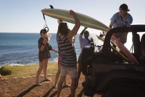 Gruppo di amici che rimuovono la tavola da surf dalla jeep in spiaggia — Foto stock