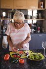 Seniorin schneidet Gemüse in Küche zu Hause — Stockfoto