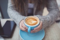 Sección media de la mujer sosteniendo la taza de café en la cafetería - foto de stock