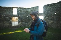Junge männliche Wanderer mit Handy in alter Ruine auf dem Land — Stockfoto