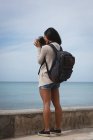 Вид ззаду жінки, що клацає фотографією моря з цифровою камерою — стокове фото