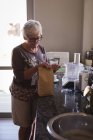 Seniorin schneidet in Küche zu Hause ein Milchpäckchen — Stockfoto