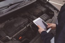 Mid section of mechanic using digital tablet at repair garage — Stock Photo