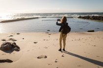 Visão traseira da mulher clicando foto do mar na praia — Fotografia de Stock