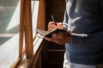 Mid section of man writing note on diary at log cabin — Stock Photo