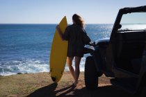 Rückansicht einer Frau, die mit Surfbrett am Strand steht — Stockfoto