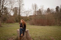 Schöne Frau benutzt Handy, während sie auf Baumstumpf sitzt — Stockfoto