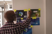 Diseñador gráfico senior mirando notas adhesivas en la oficina - foto de stock
