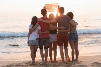 Group of friends holding american flag in the beach at dusk — Stock Photo