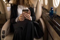 Средняя секция деловой женщины, использующей мобильный телефон в частном самолете — стоковое фото