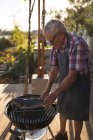 Uomo anziano che cucina pesce sul barbecue nel cortile — Foto stock